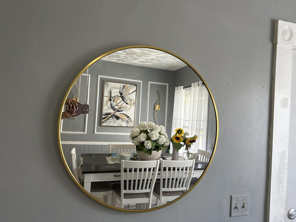 Round gold-framed mirror on a gray wall reflecting a dining room with a table and chairs.