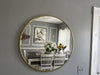 Round gold-framed mirror on a gray wall reflecting a dining room with a table and chairs.