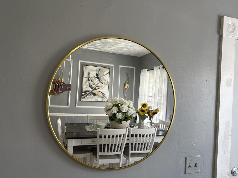 Round gold-framed mirror on a gray wall reflecting a dining room with a table and chairs.