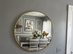 Round gold-framed mirror on a gray wall reflecting a dining room with a table and chairs.