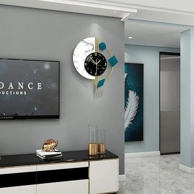 Modern wall clock on a gray wall above a black and white cabinet with a television displaying 'DANCE' in the background.