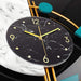 Wall clock with black marble design and gold accents on a marble surface